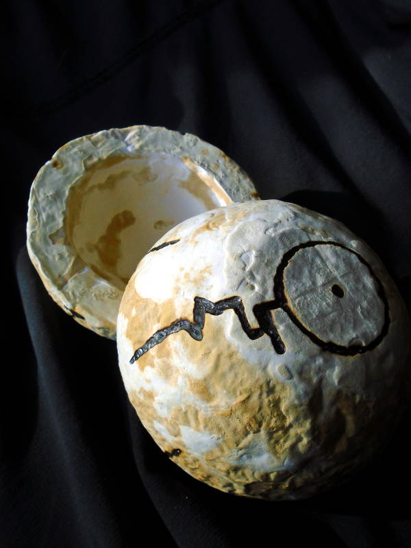 Two hollow hemispheres made of mycelium. A black glyph has been burned into the exterior surface of one of the hemispheres.